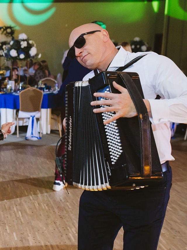 Akordeonista gra na parkiecie wśród roześmianych gości weselnych