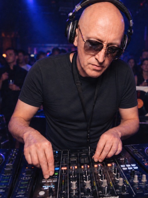 Paweł Brzeźnicki w słuchawkach za konsoletą DJ-ską, w tle rozświetlony parkiet